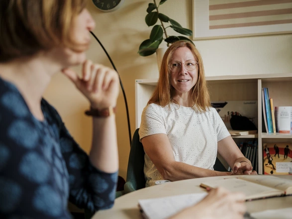 Zwei Mitarbeiterinnen des CJD sprechen gemeinsam und notieren in Notizbüchern vor ihnen auf dem Tisch.